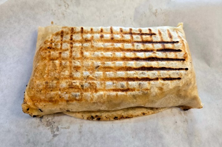 A rectangular brick of flour tortilla encasing the ingredients that make up a French tacos.