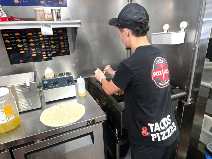A man in a black shirt and cap cooking on a griddle next to a flour tortilla