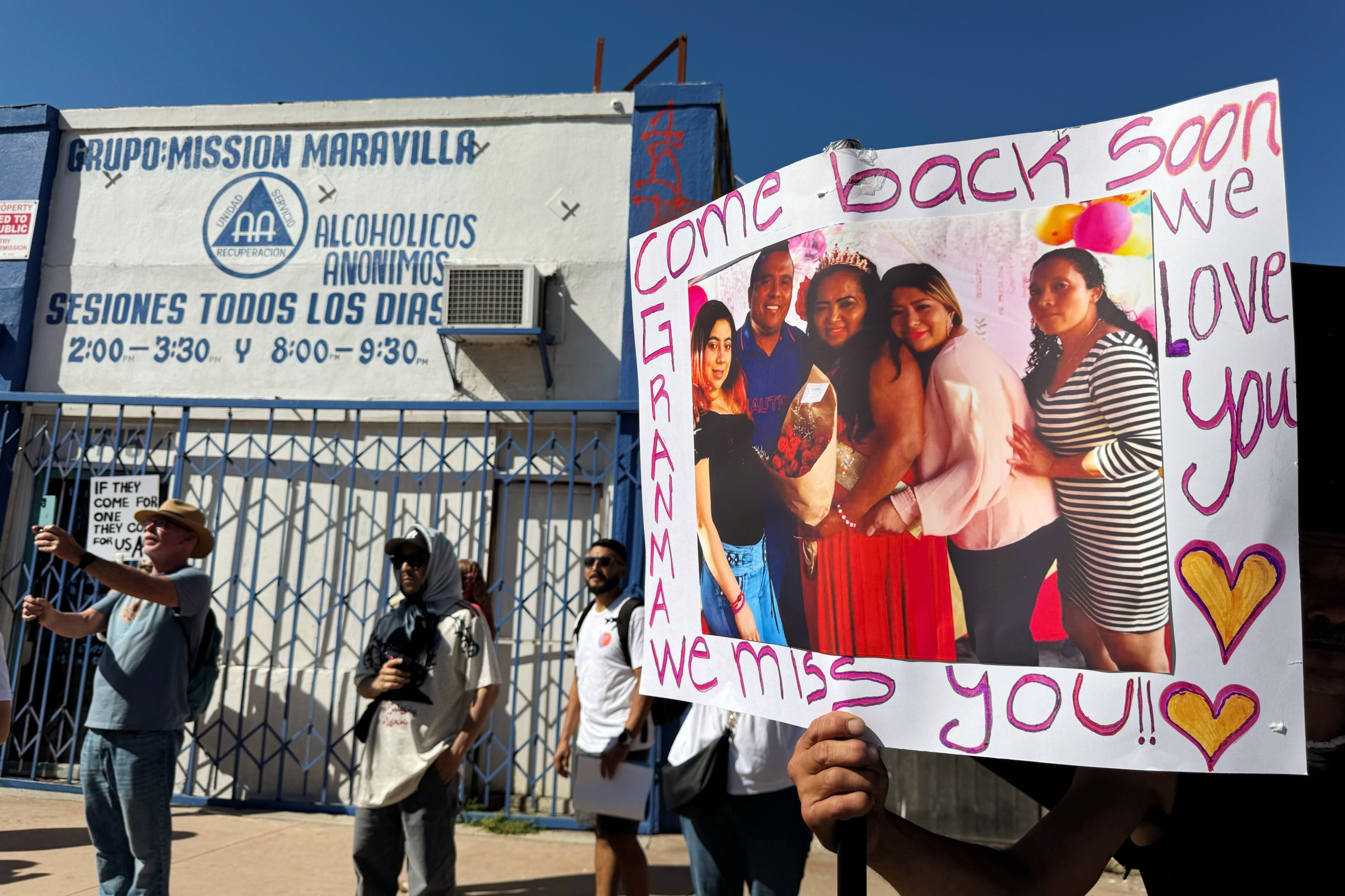 A family member of street vendor organizer Emma De Paz holds up a poster with his grandmother's photo. The words "Come back soon" and "We Miss You" are written across the poster.