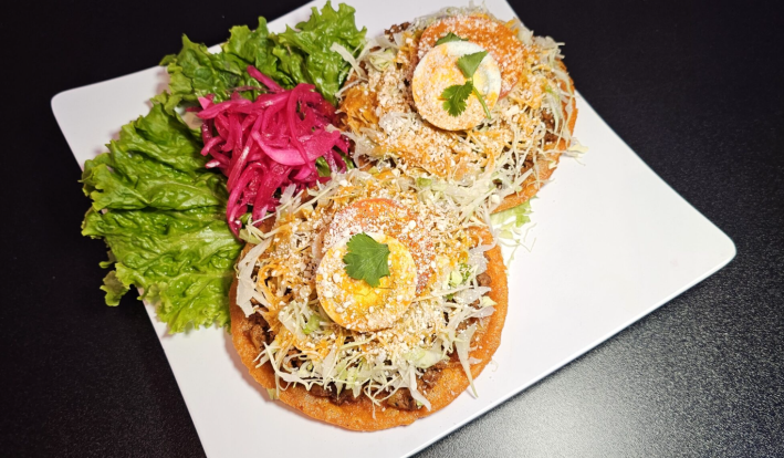 Enchiladas with meat, lettuce, cheese and topped with slices of boiled egg and tomato.
