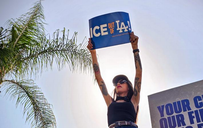 A protestor at Dodger Stadium holding an ICE Out of LA sign.