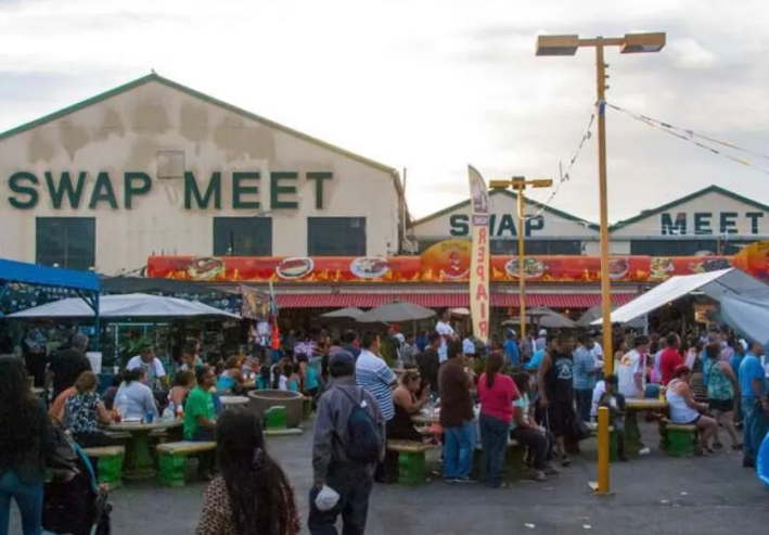 A sign for the Alameda Swap Meet over a busy daytime market of street vendors