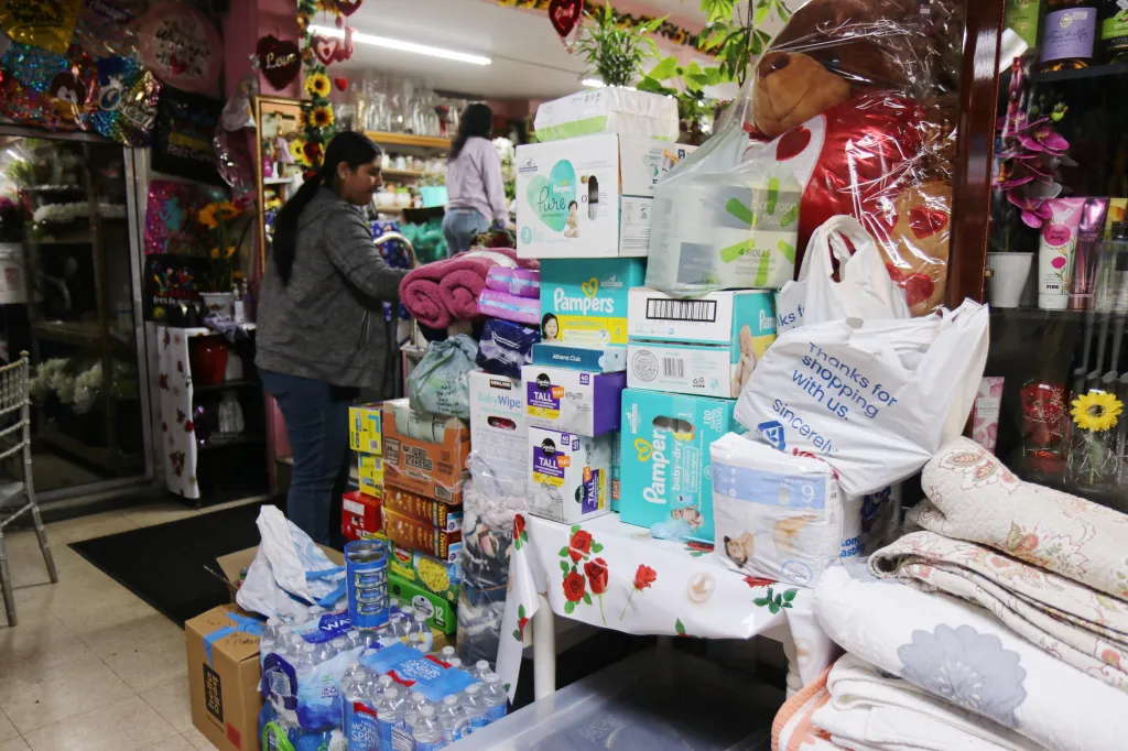A volunteer helps organize supplies behind a small mountain of diapers and water bottles