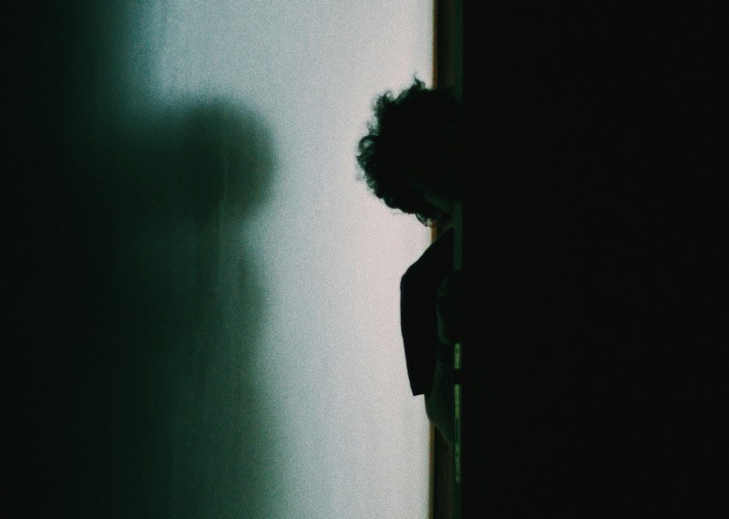 a person looks around a corner in shadow