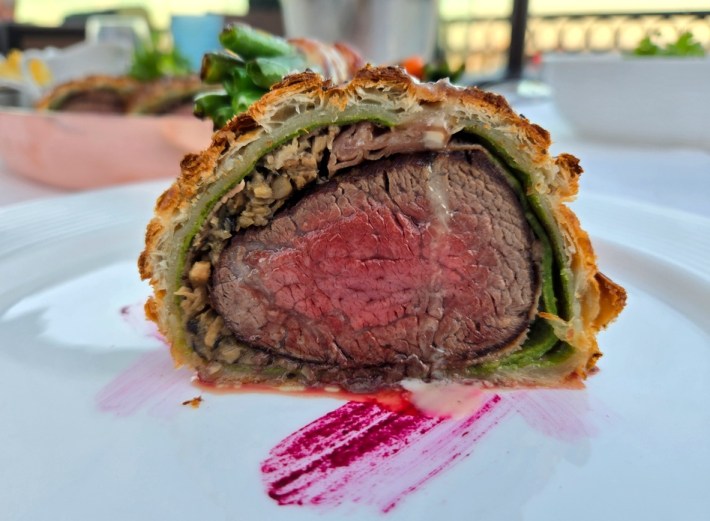 A slice of beef wellington, with a smear of bright red sauce in front of it on the white plate