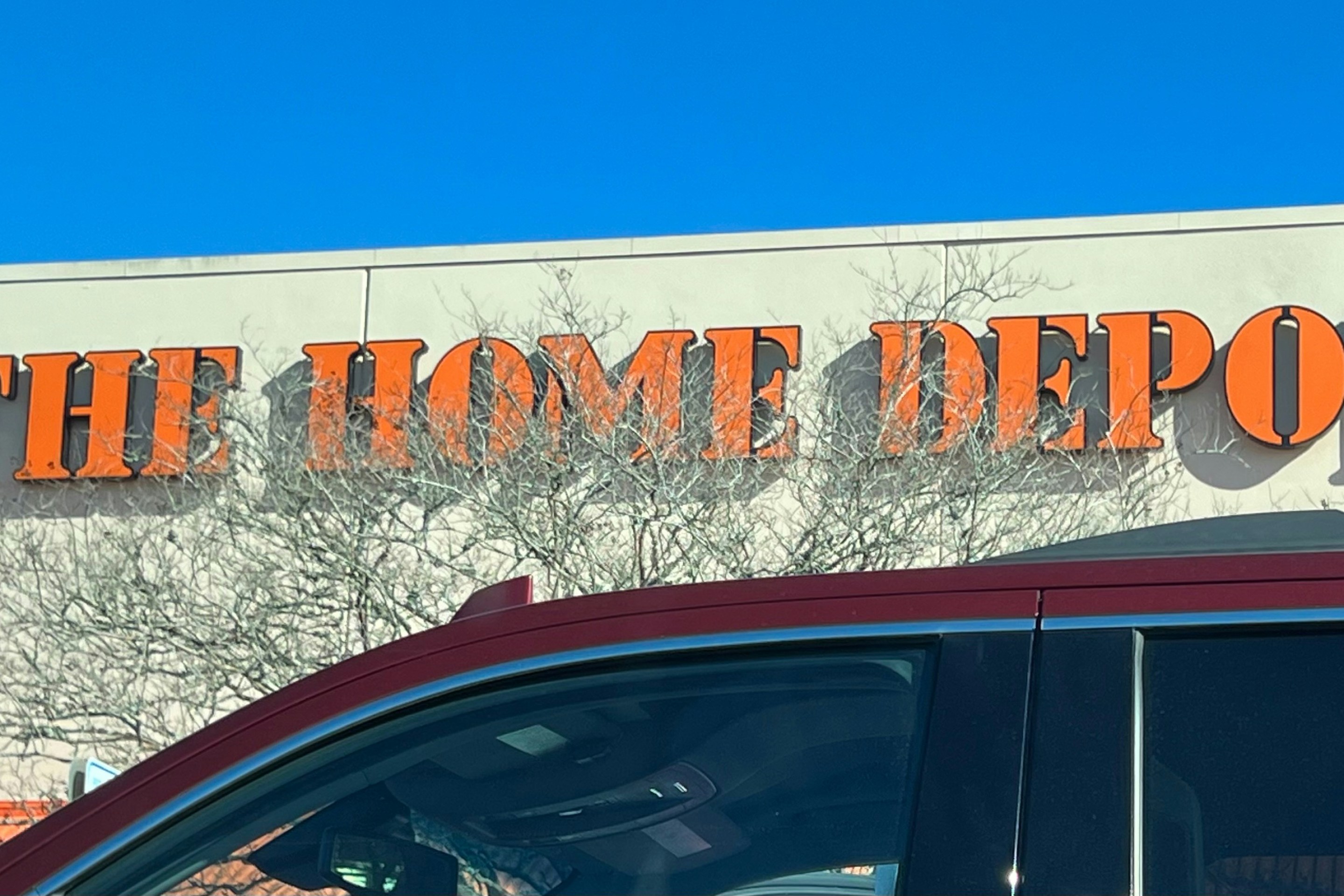 A Home Depot sign and roof in front of a blue sky, with car windows passing below
