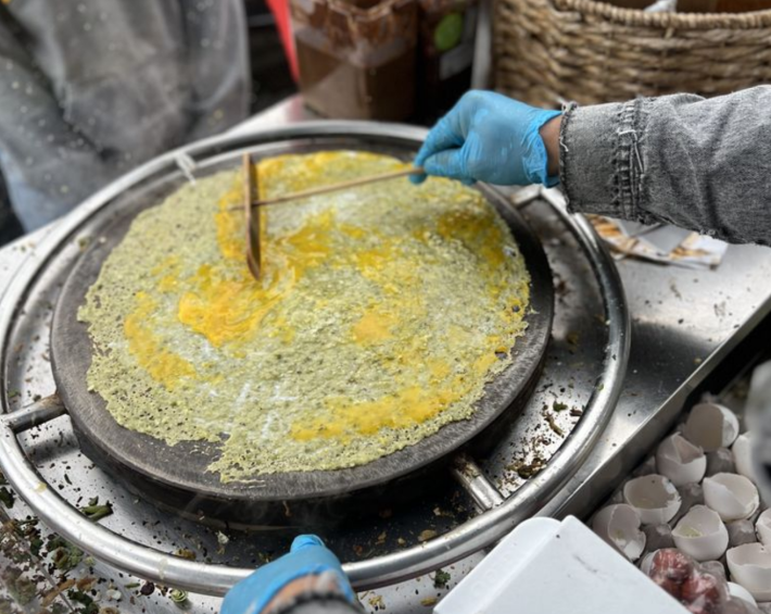 A pale yellow Chinese crepe spread across a circular grill