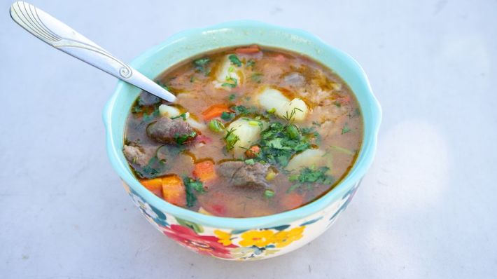 Rezushurba stew wtih carrots, potato, and parsley in a bowl decorated with painted flowers and a spoon sticking out of its side