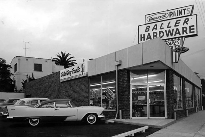 A black-and-white photo of Baller Hardware with a classic car parked in front