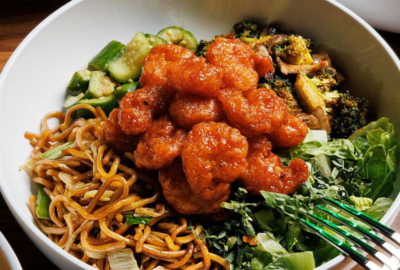 Orange-mango chicken on noodles with salad on the side of the bowl and a fork digging in