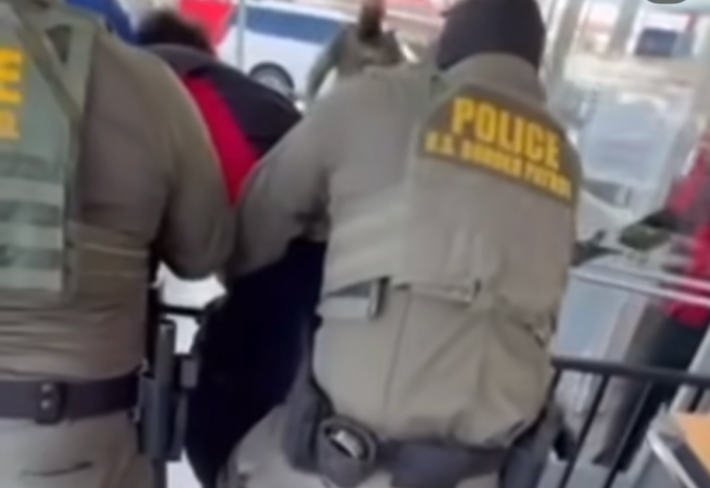 two armed border patrol agents from behind. one is seemingly holding onto a young man