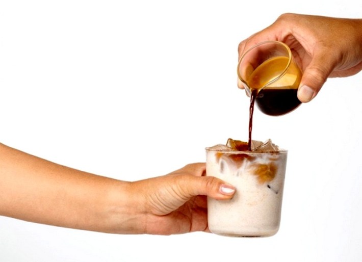 A hand pours espresso into an icy glass of horchata, which is held in the hand of an outstretched arm
