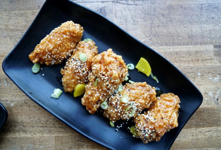5 honey garlic wings on a black platter with two yellow radish slices on the side