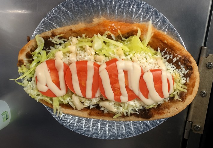 A huarache topped with cheese, lettuce, tomato, and crema