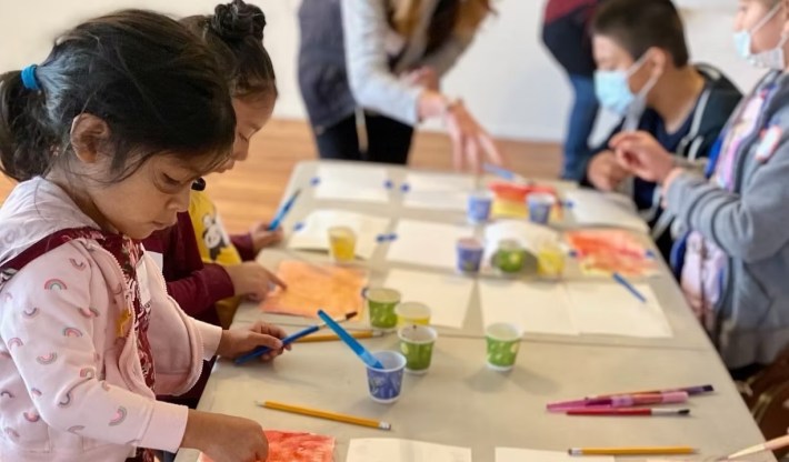 children sit together at a table painting