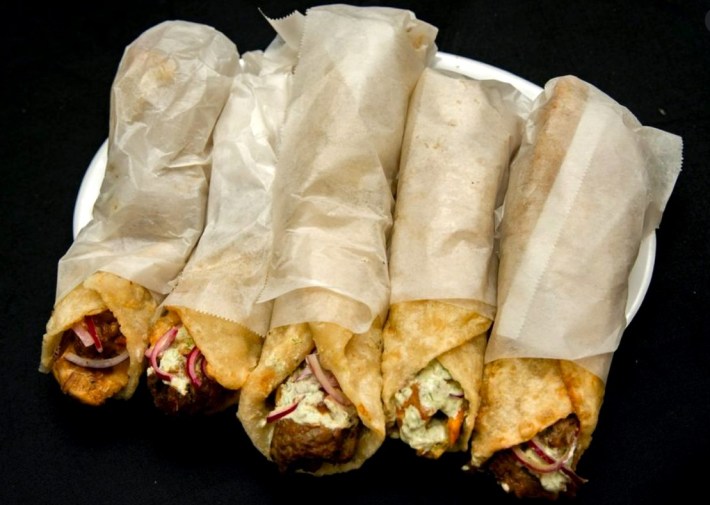 5 paratha-wrapped kathi rolls, wrapped in paper, their meat and sauces poking out of one end
