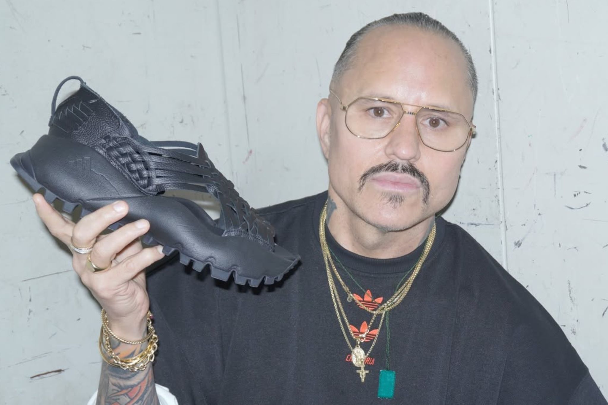 Fashion designer willy chavarria holding a huarache in one hand.