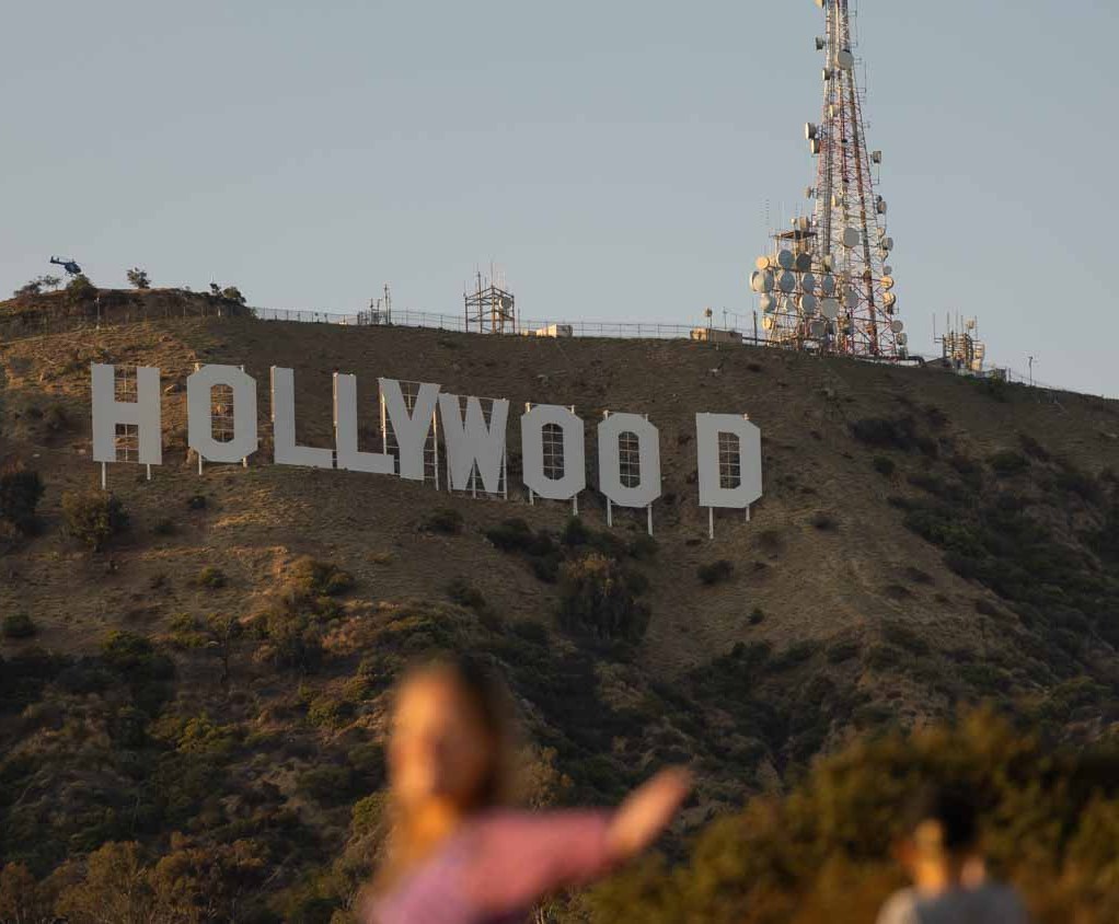 A woman poses in front of the Hollywood sign, but is blurry