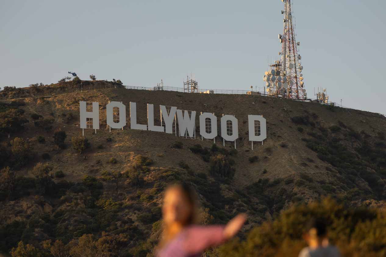 A woman poses in front of the Hollywood sign, but is blurry