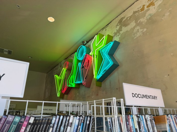 Vidiots’ trademark neon sign glows behind the documentary shelf