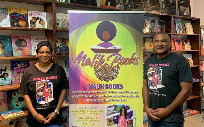 The owners of Malik Books stand next to a yellow poster about Malik Books