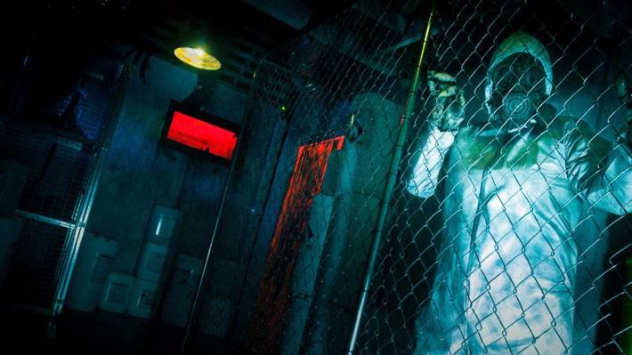 A man in a haz-mat suit clings to a fence in a dark room