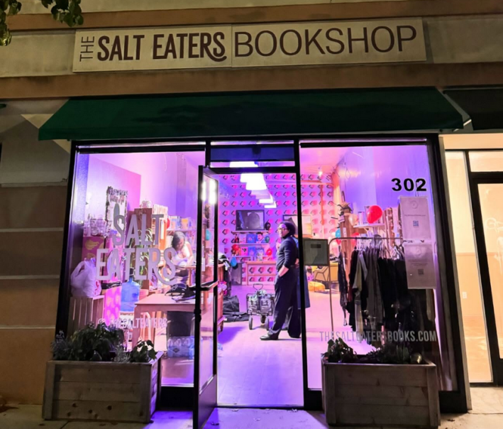 An exterior shot of The Salt Eaters Bookshop with a woman inside visible through the glass and purple lighting