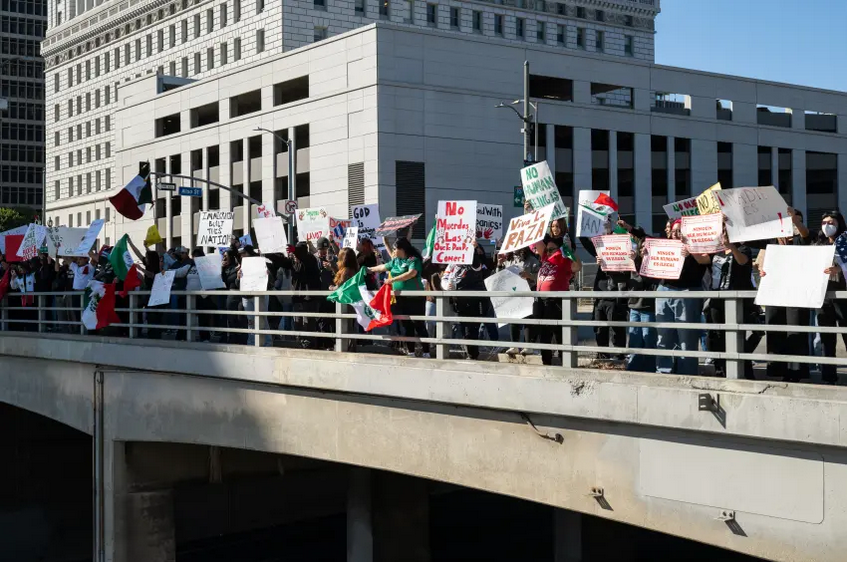 Protestors hold signs and a Mexican flag over the 101 Freeway in Downtown L.A>