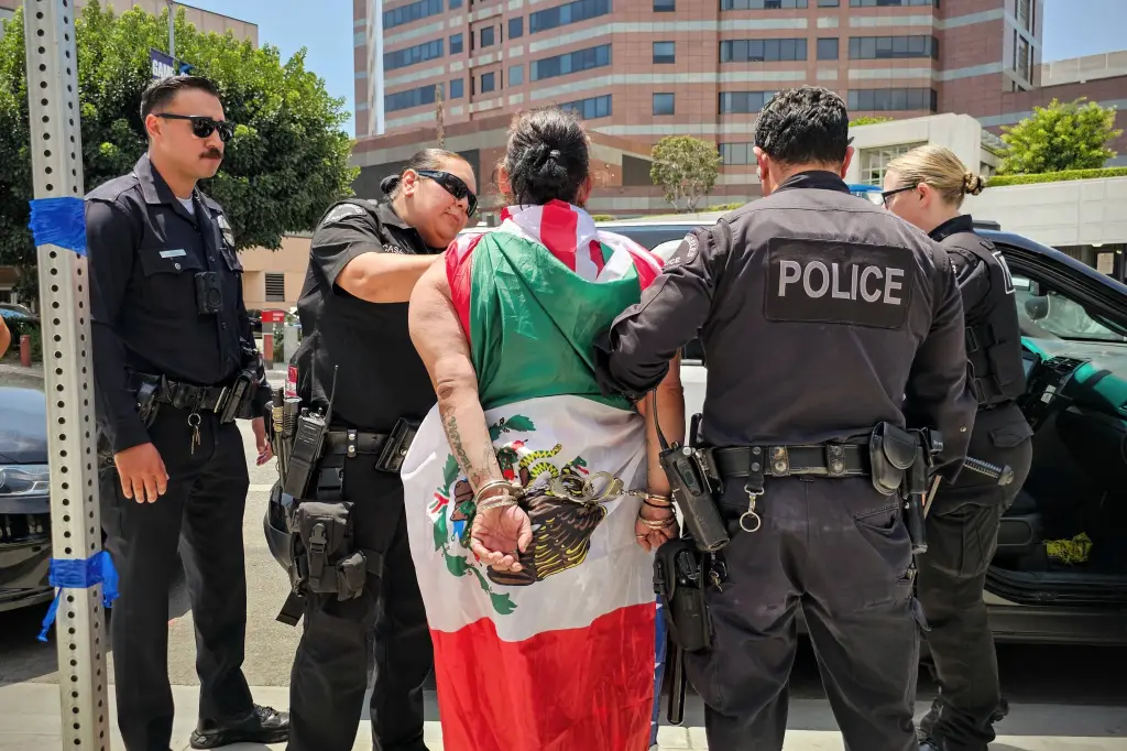 A woman draped in a Mexican flag being led away in handcuffs