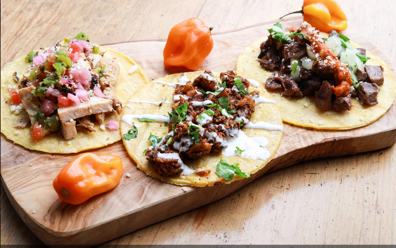 Tacos de pollo, pastor, and filet mignon on a serving board with two chiles on it