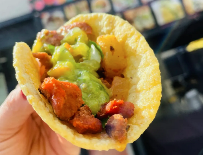 A yellow corn taco with potates, chicken tinga, and guacamole in someone's hand