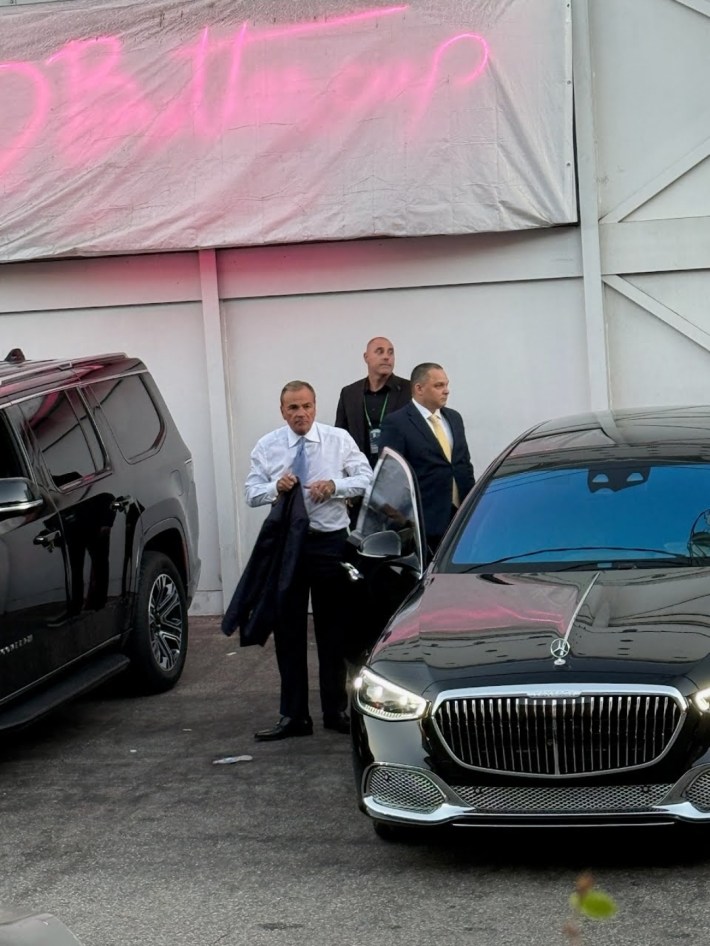Rick Caruso stands wearing a suit next to a Mercedes with two men behind him.
