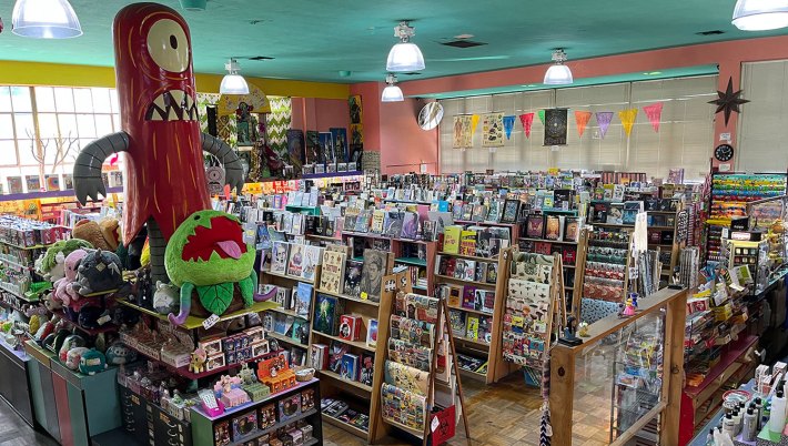 A crazy gift and book store with an inflatable red monster and plush man-eating plant emerging from the shelves
