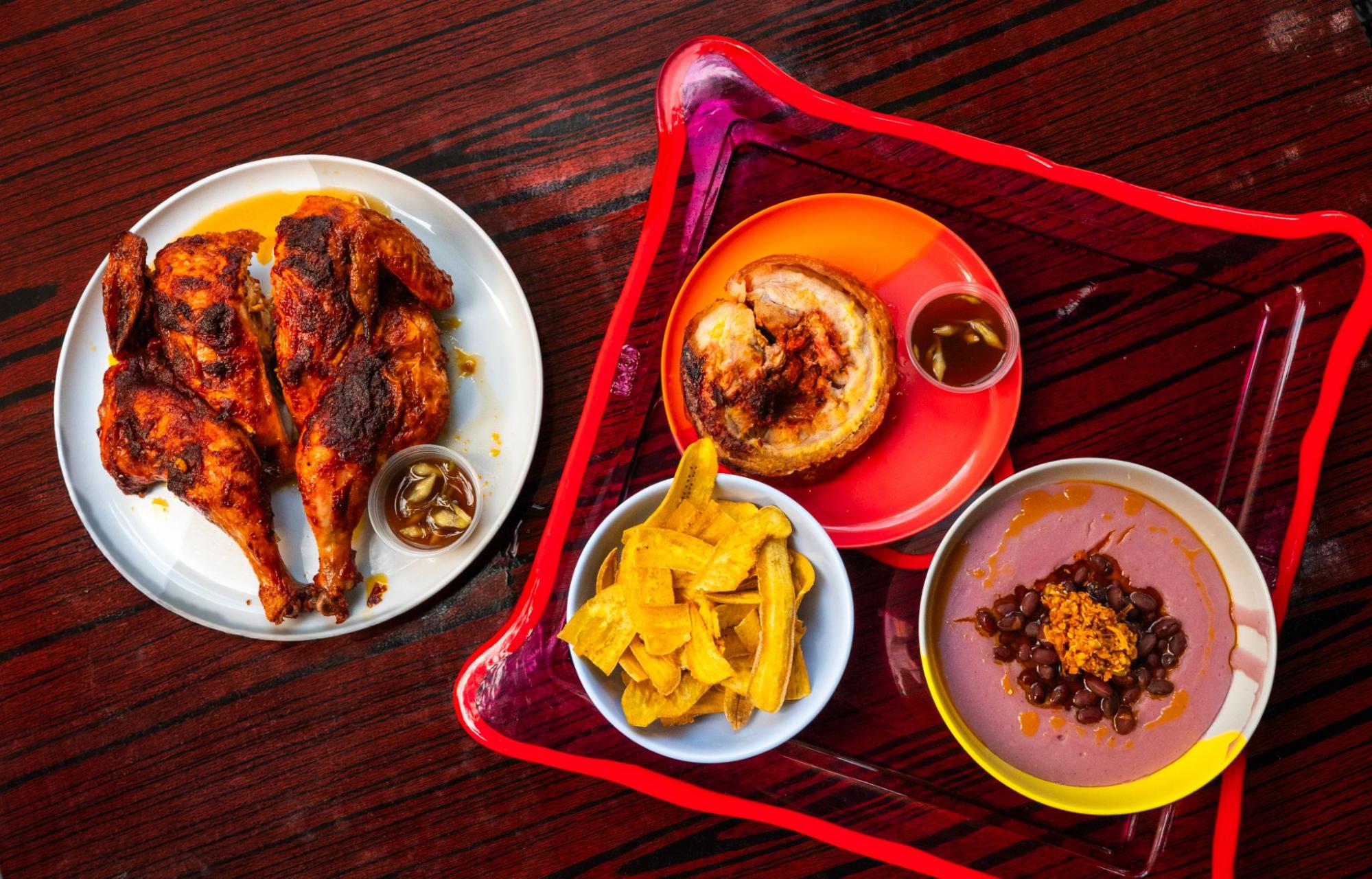 A table set with chicken and a tray holding various modern Salvadoran dishes including yucca frita