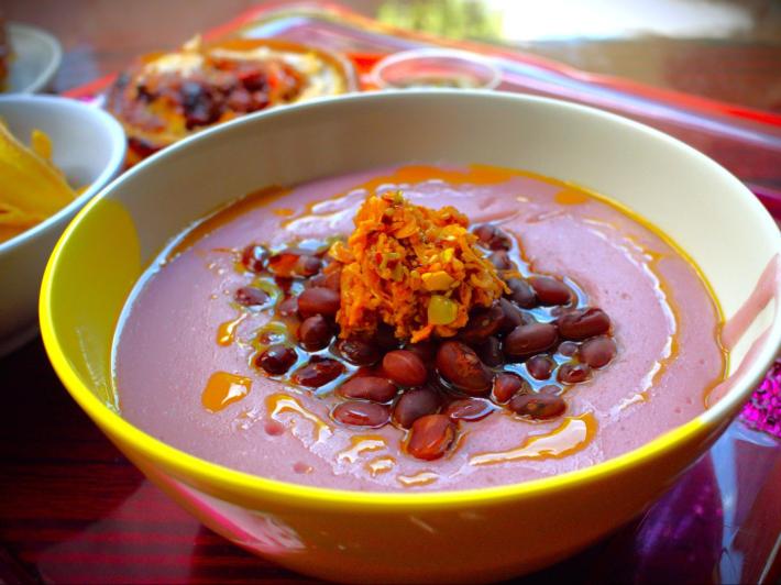 A bowl of red broth topped with beans and orange, shredded pickles