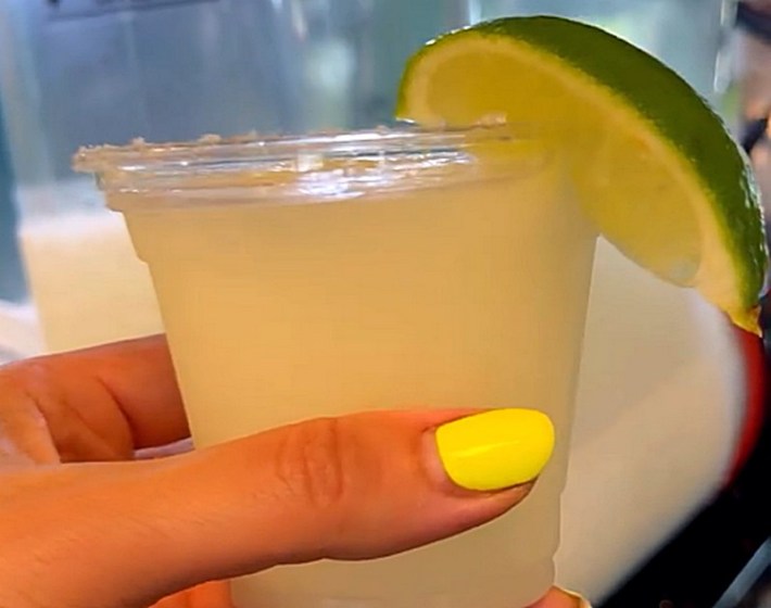 A frozen margarita with a lime wedge in a hand with yellow-painted fingernails