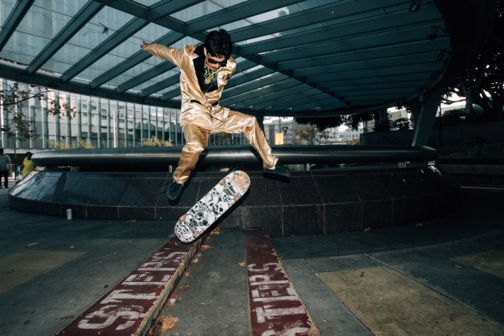 A skater in a gold outfit does a flip in the air.