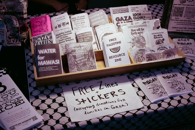 Multiple free paper zines are displayed on a stand on a table covered by a keffiyeh. The zines are about topics like pro-Palestinian movements and anti-ICE resources.