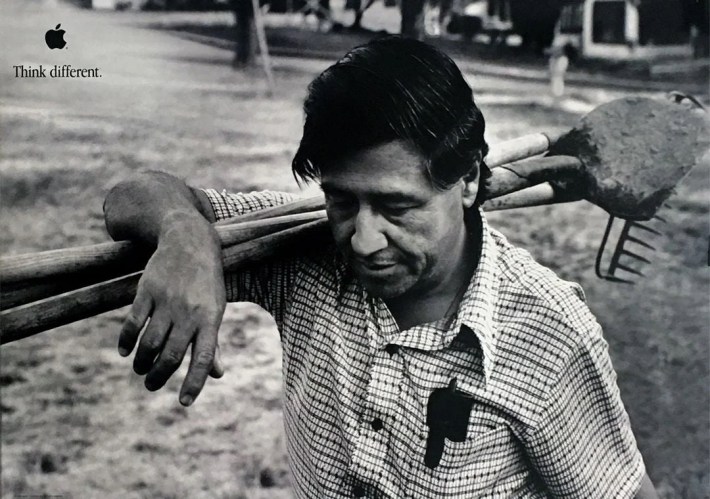 A man looks down while holding farming tools on his shoulder.