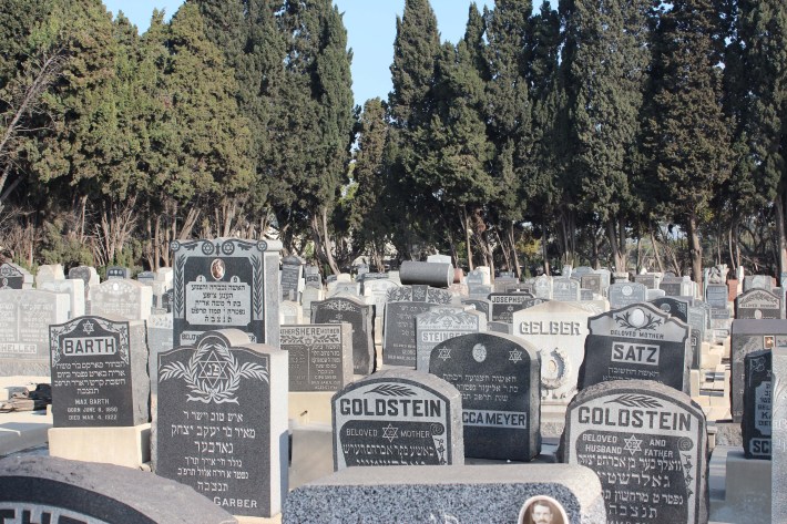 Many gravestones featuring Hebrew are shown in a cemetery.