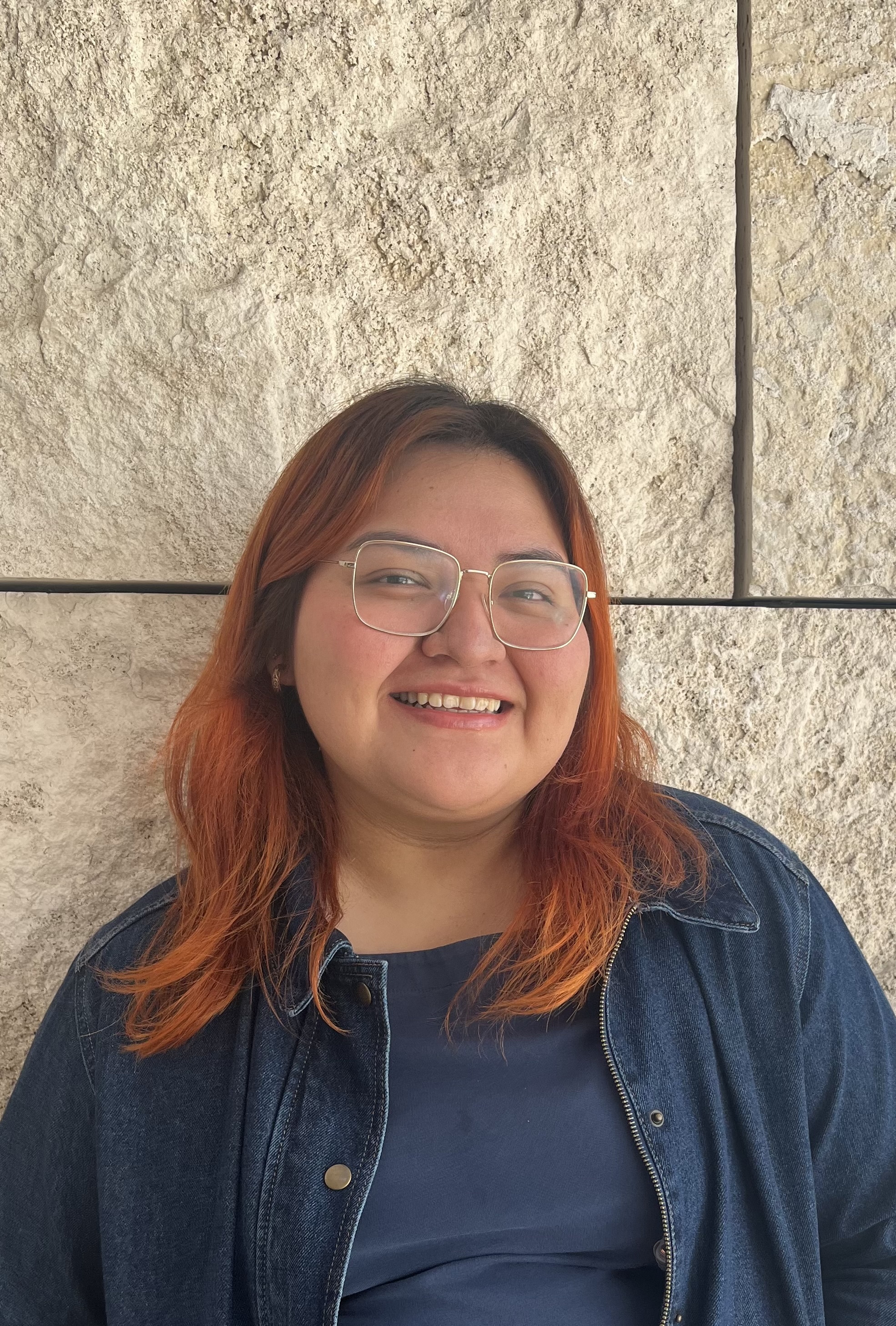 a woman with red dyed hair and glasses smiles