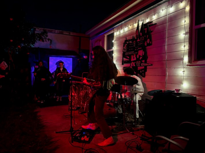 A man with long hair plays bass in front of a drummer