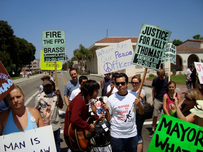 A group of people protesting police brutality, with a man with a guitar in the middle