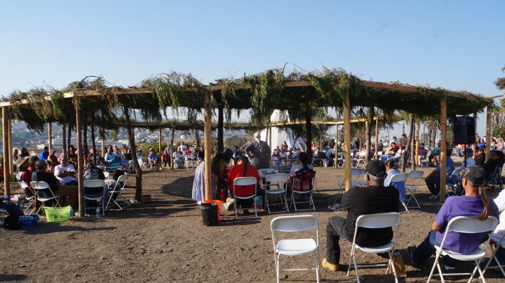 Community members gather in a circle while sitting on white chairs.