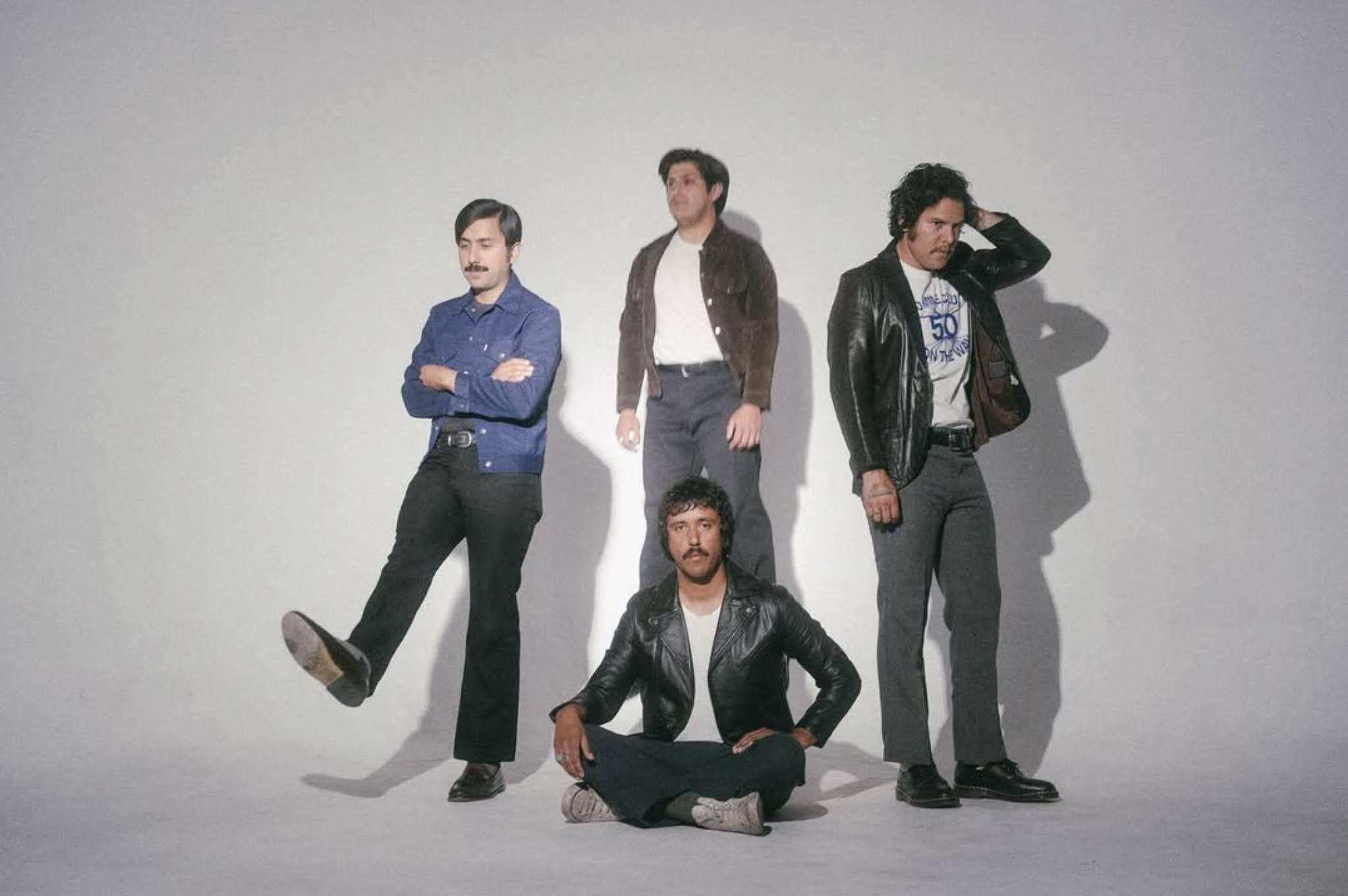 A band, Levitation Room, are pictured together. Four bandmates pose playfully in front of a white background.