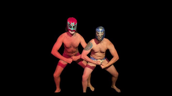 Two masked, shirtless luchadors flex for the camera
