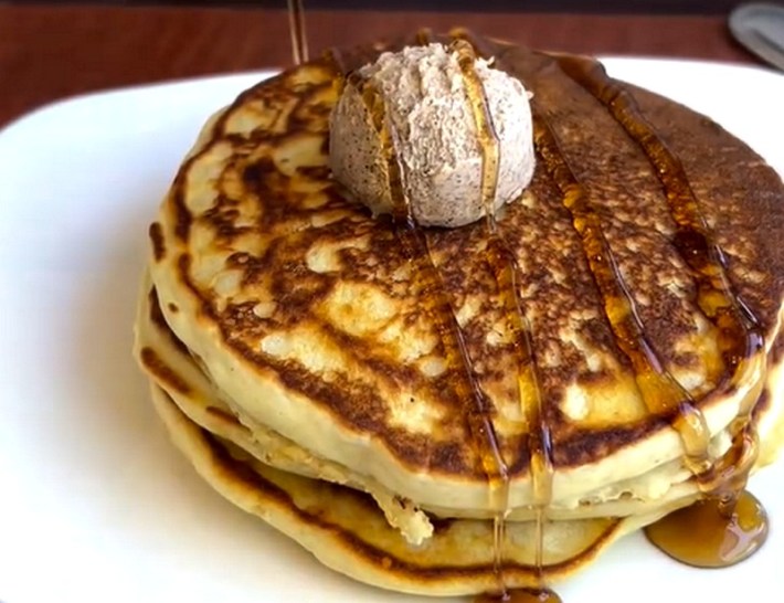 A stack of masa pancakes drizzled with syrup and a big ball of butter on top