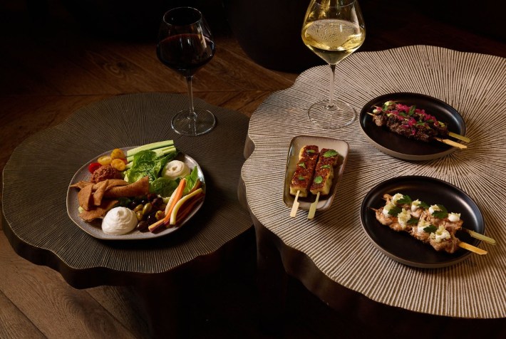 Skewers of Wagyu, chicken, and halloumi, and a mezze plate, next to two glasses of wine