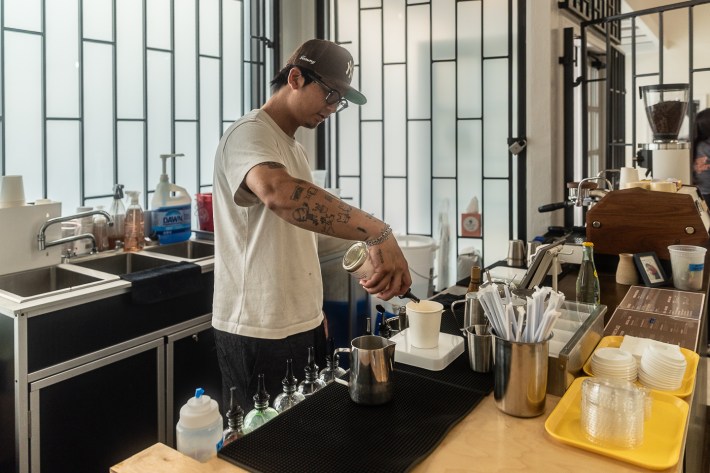 A man behind a coffee bar makes a drink.