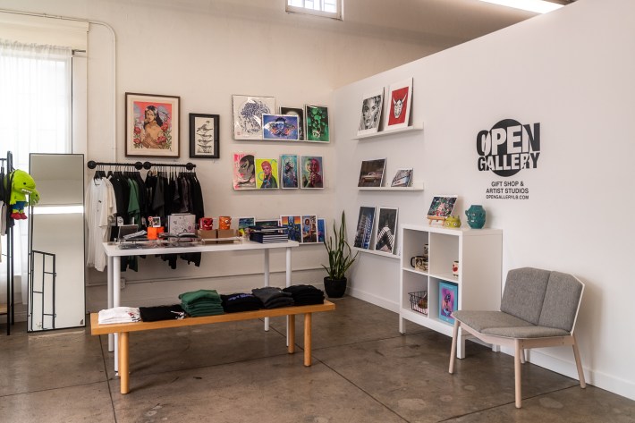 The Open Gallery gift shop is depicted; some items for sale are prints, shirts, and mugs.